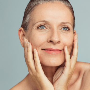 Woman with clear skin touching her face against a gray background